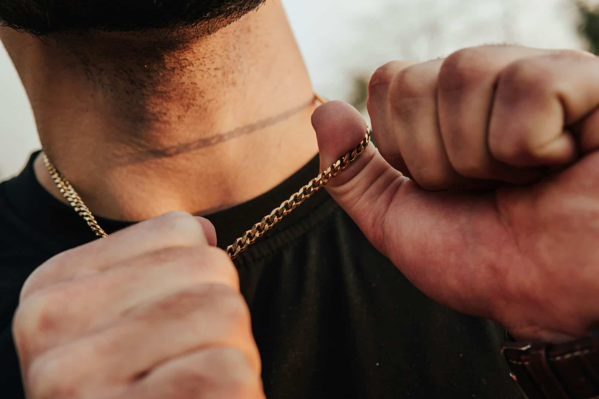Close up of a man wearing a black t shirt holding his gold chain necklace